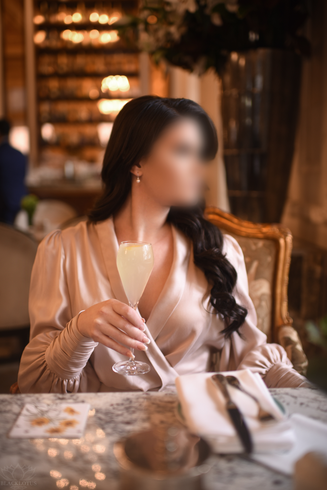 Woman in elegant champagne silk blouse enjoying white wine at upscale restaurant with warm ambient lighting