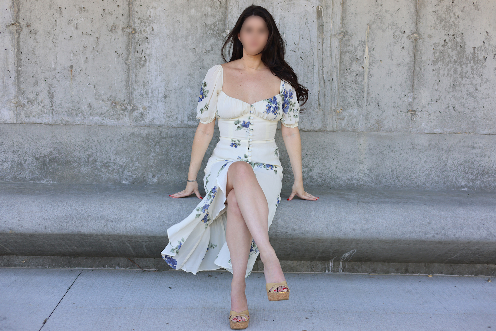 Woman in white floral dress sitting on concrete steps against industrial wall in elegant lifestyle portrait