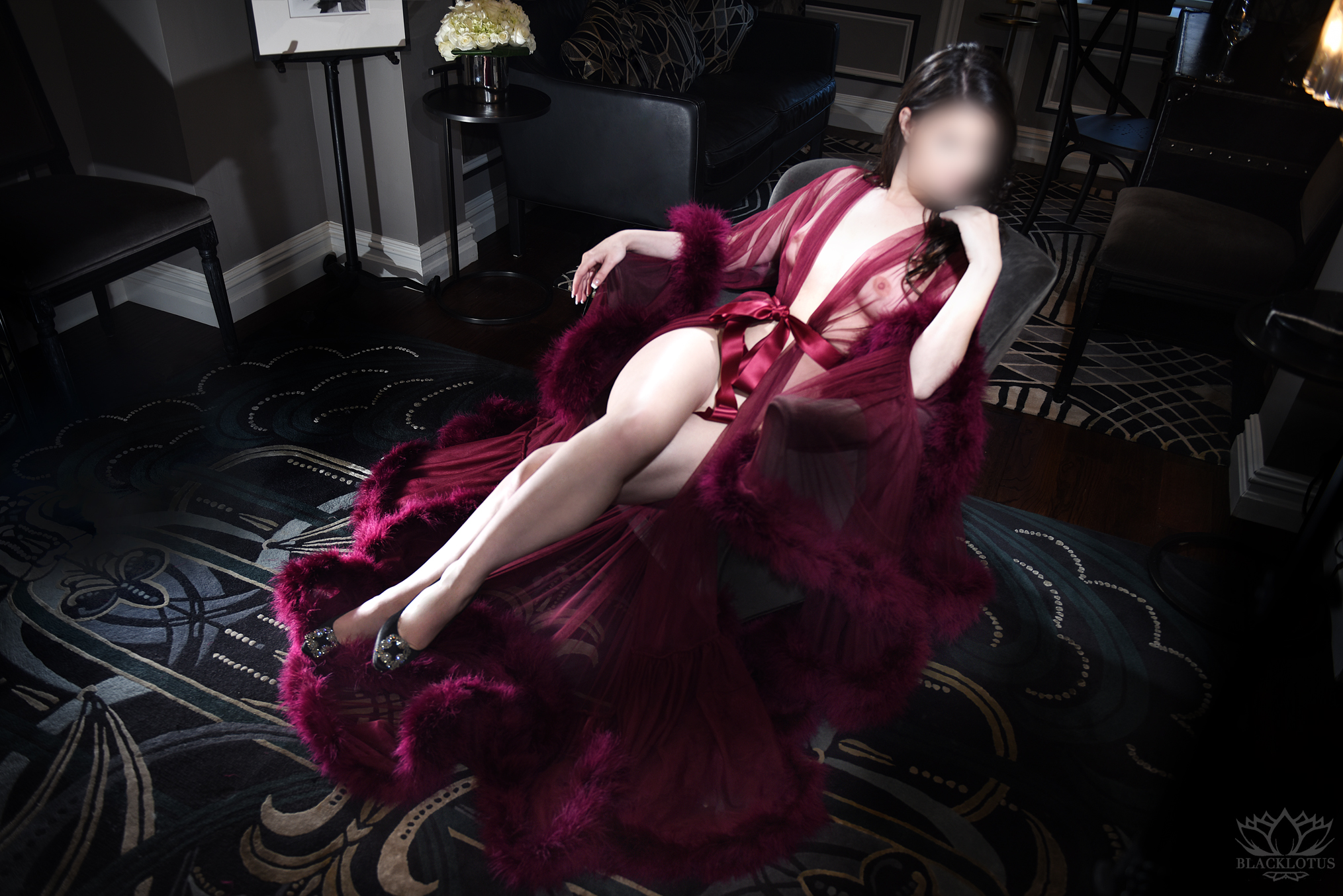 Woman in luxurious burgundy silk gown with feather trim reclining on ornate black carpet in elegant interior setting