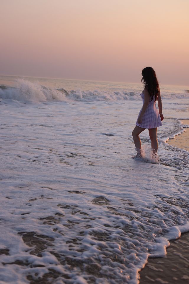 Woman in white dress walking through ocean waves at sunset on a serene beach